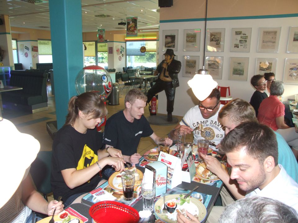 Group of people eating at tables in a diner with a statue of a man in a hat and leather jacket