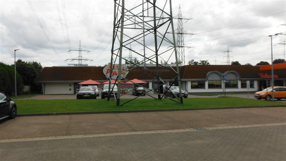 Several cars parked in front of a building, with a large power line tower dominating the foreground