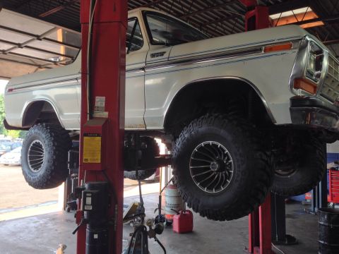 1979 Ford Bronco - A white Ford Bronco is raised on a car lift, revealing its modified suspension and off-road tires.