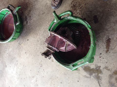 1979 Ford Bronco - A broken differential housing and gears sit in a green fluid drain pan on a concrete floor.