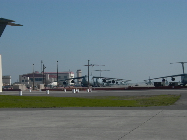 Several large military cargo planes parked on an airfield with buildings in the background