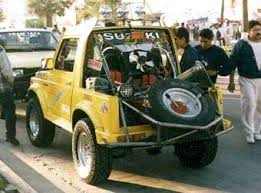1987 Suzuki Samurai - A yellow 1987 Suzuki Samurai is shown from the rear, equipped with a spare tire and roll cage.