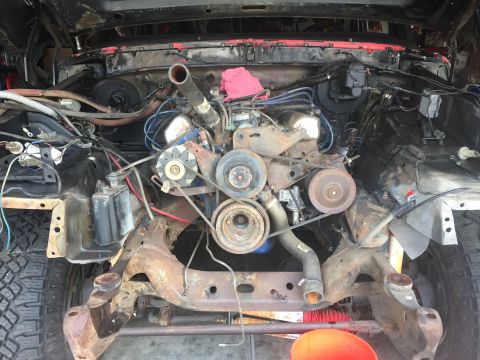 1978 Ford Bronco - The engine bay of a vehicle, showing the V8 engine and surrounding components, with visible rust on the chassis.