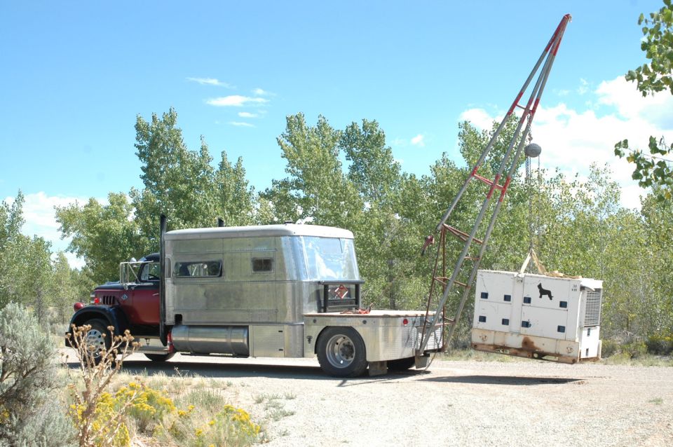 Custom truck with a silver camper shell and a crane lifting a white crate with dog silhouettes