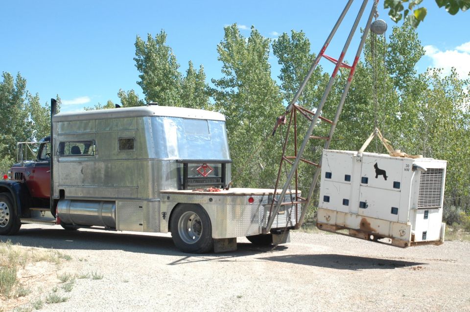 Custom truck with silver Airstream-style cabin, flatbed, and a crane lifting a white container with a dog silhouette