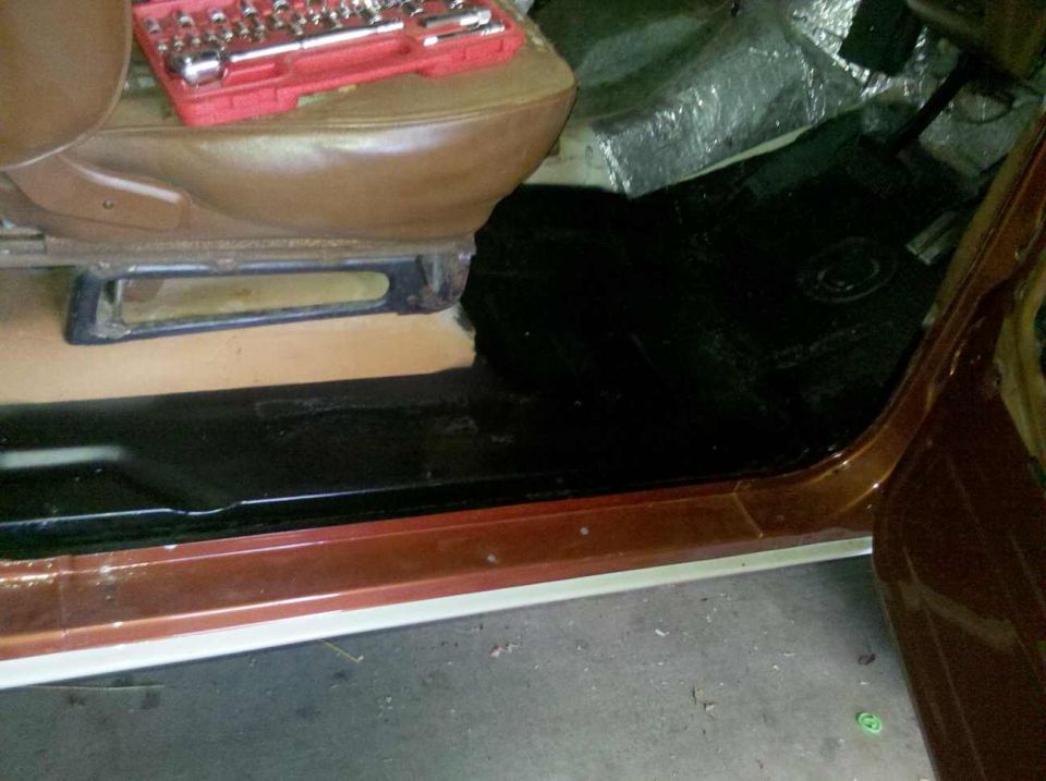 Interior view of a vehicle with a socket set on the seat, showing floor and door sill during repair