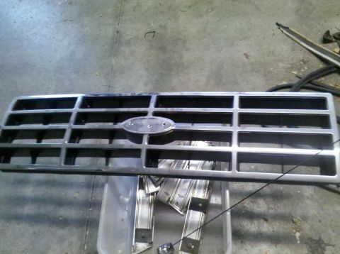 1982 Ford Bronco - A chrome grille with a Ford emblem sits in a workshop, ready for installation or repair.