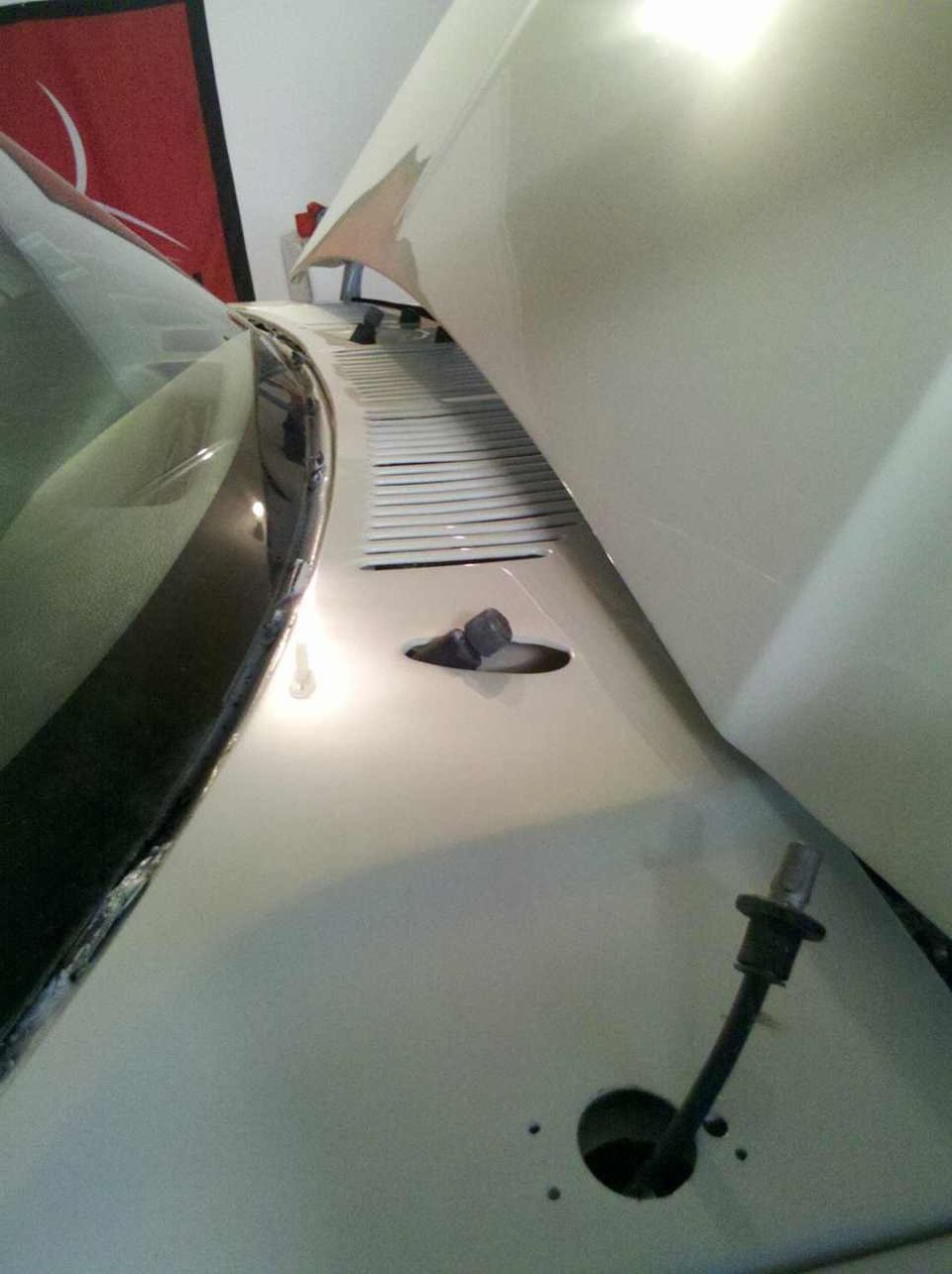 White car hood with louvers and windshield wiper base. Hood is open