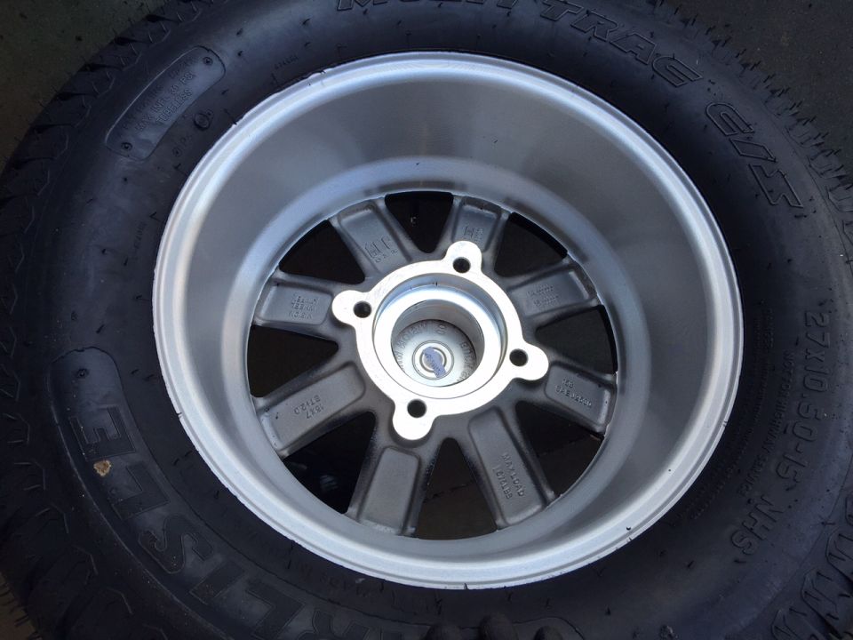 Close-up of a silver 5-spoke alloy wheel with a black tire. Tire has size 275/60-15