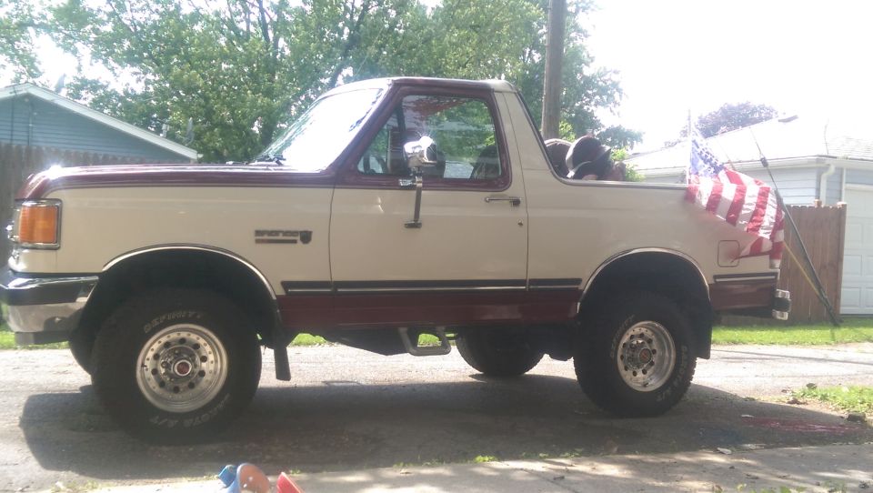 1988 Ford Bronco parked in driveway, side view, American flag on rear