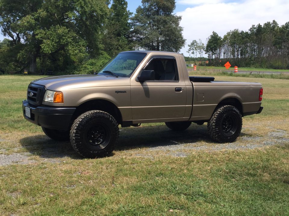 Tan Ford Ranger pickup truck with black off-road tires parked on grass