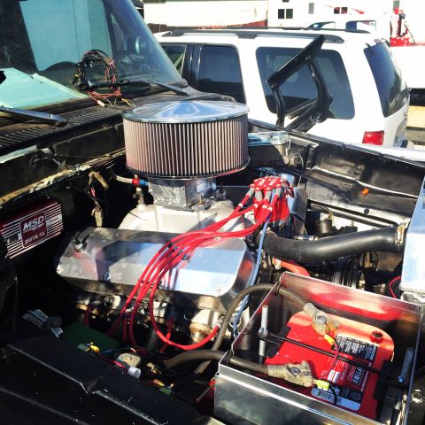 1979 Ford Bronco - The engine bay of a vehicle shows a V8 engine with custom modifications and a red battery.