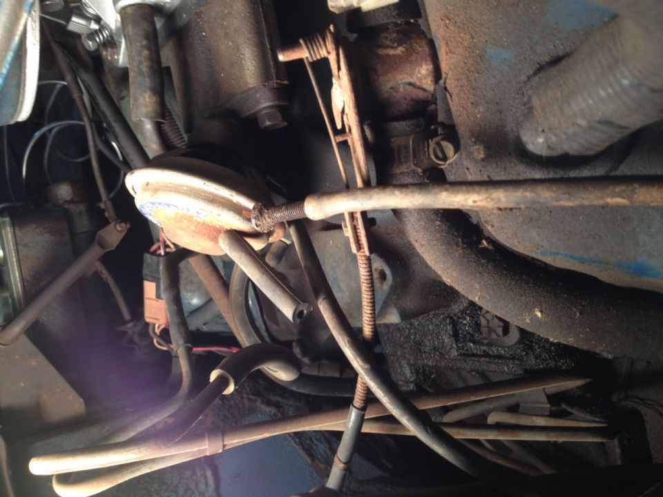 Engine bay with hoses, cables, and rusty metal parts. A blue painted surface is visible