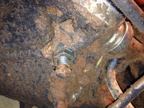 1973 Ford Bronco - Close-up of a heavily corroded bolt and surrounding metal parts, covered in mud.