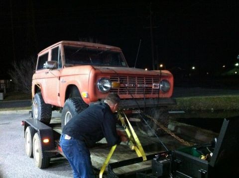 1974 Ford Bronco - A man secures an orange 1974 Ford Bronco onto a trailer at night.