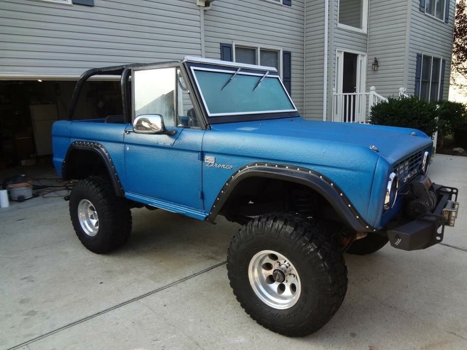 Blue Ford Bronco with aftermarket bumper and winch parked in a driveway