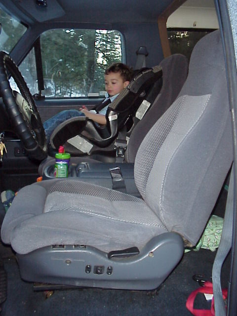 1989 Ford Bronco - Interior shot through the open passenger door showing a gray cloth bucket seat with two-tone woven inserts and power-adjust switches on the…