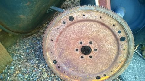 1994 Ford Bronco - A heavily rusted flywheel sits on gravel next to a dark green object.