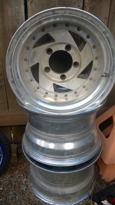 1994 Ford Bronco - Three aluminum alloy wheels are stacked on top of each other outdoors.
