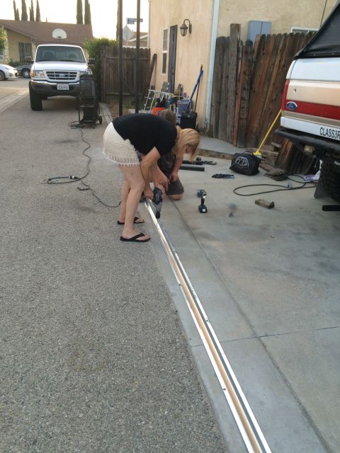 1968 Ford Mustang - Two people are working on a metal track in a driveway, with a white Ford pickup truck visible.