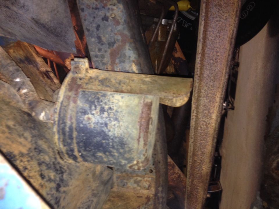rusted metal bracket attached to a dark cylindrical component, part of a vehicle's undercarriage