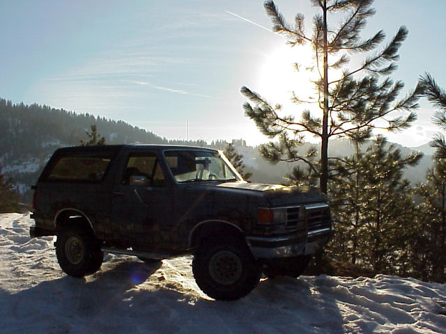 Dark blue Ford Bronco parked on a snowy hillside, sun glinting off the windshield