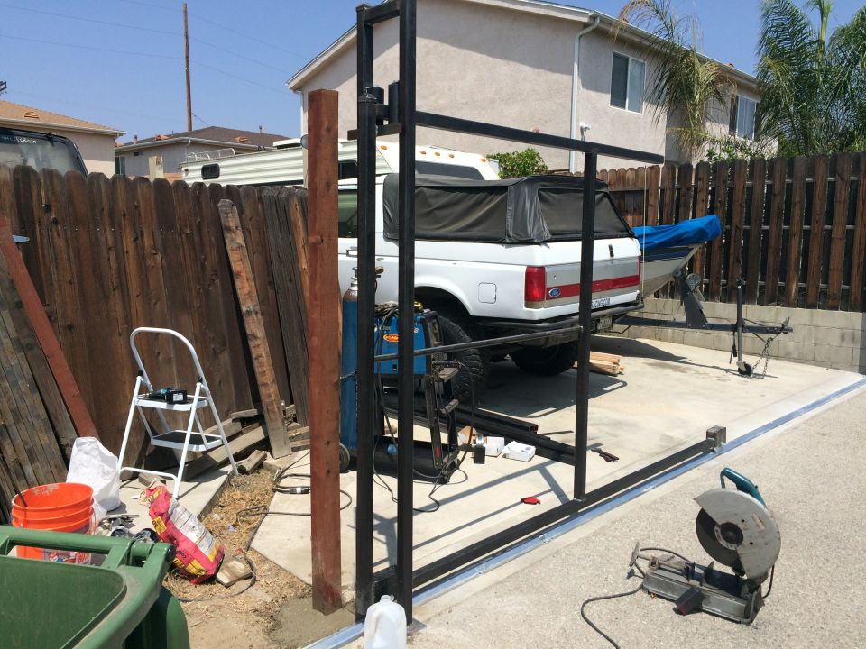 White Ford pickup truck with a black camper shell, towing a boat trailer. Construction materials and tools are in the foreground