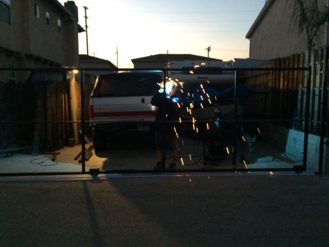 1968 Ford Mustang - A person welds a gate in front of a pickup truck with a camper shell at dusk.