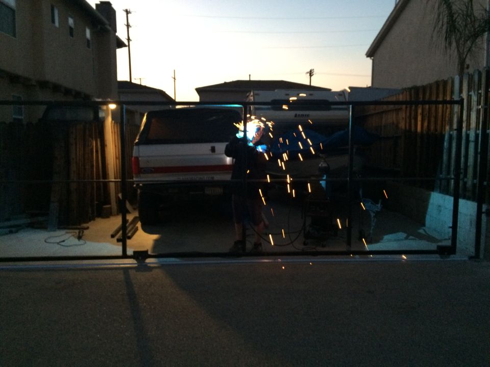 Rear view of a pickup truck with a camper shell, as a person welds a gate