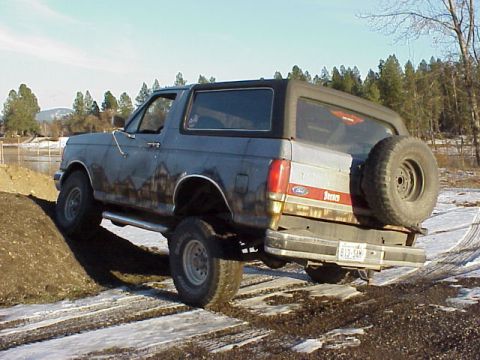 1989 Ford Bronco - This 1989 Ford Bronco is shown from the rear, navigating an off-road terrain with muddy conditions.