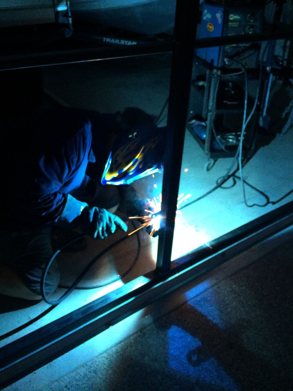 Person wearing a welding mask and gloves, sparks flying as they weld a metal frame
