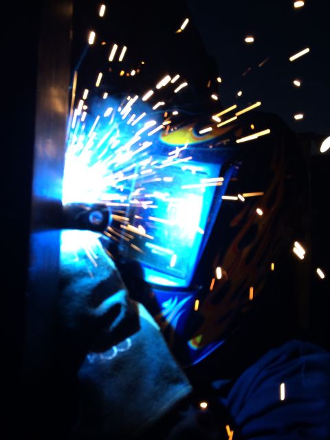 1968 Ford Mustang - A welder works in the dark, surrounded by a shower of bright orange sparks from the welding torch.