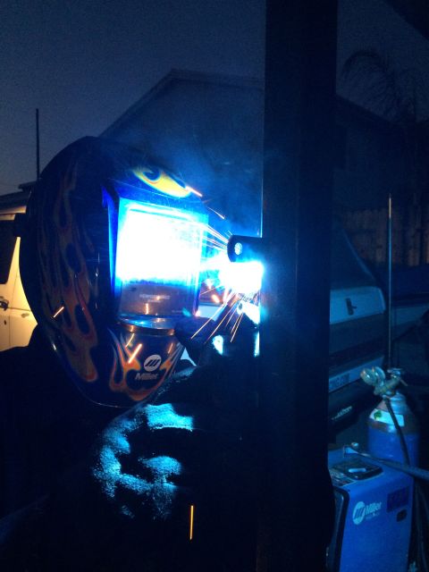 1968 Ford Mustang - A welder in a flame-patterned helmet works under the cover of darkness, with a white vehicle visible in the background.
