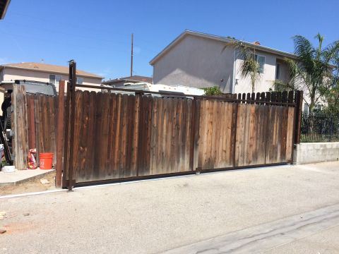 1968 Ford Mustang - A weathered wooden gate stands closed in a residential driveway under a clear blue sky.