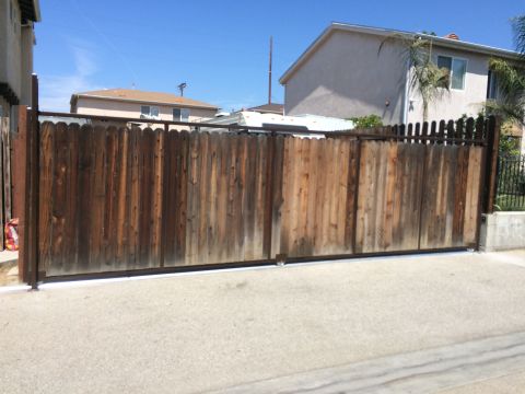 1968 Ford Mustang - A wide, weathered wooden gate spans a driveway in front of residential buildings under a clear blue sky.