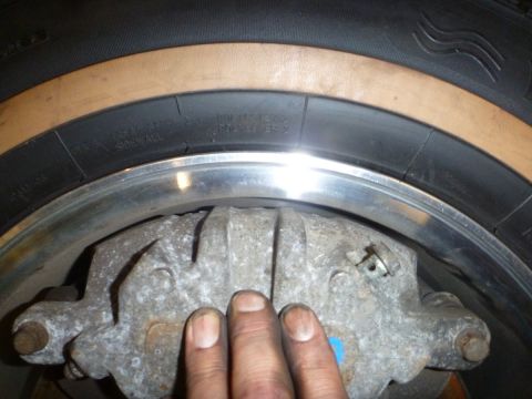 1964 Mercury Monterey - A close-up view of a vehicle's brake caliper and tire, with a hand obscuring part of the caliper.