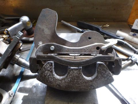 1964 Mercury Monterey - Brake caliper assembly with pads, clamped in a vise on a workbench with tools.