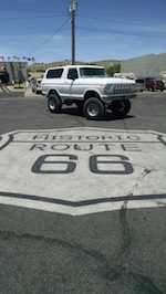 1979 Ford Bronco - White 1978 Ford Bronco lifted on large tires, parked on Historic Route 66 pavement. Super Motors logo visible.