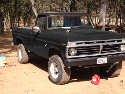 1987 Ford Bronco - This vintage Ford pickup truck is parked in a dirt lot with trees and firewood visible.
