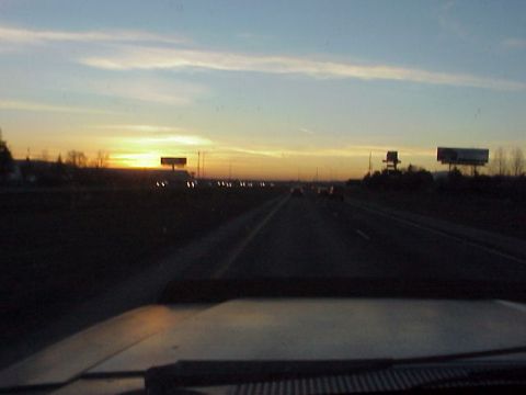 1989 Ford Bronco - View from inside a vehicle driving on a highway as the sun sets, with traffic and billboards visible.