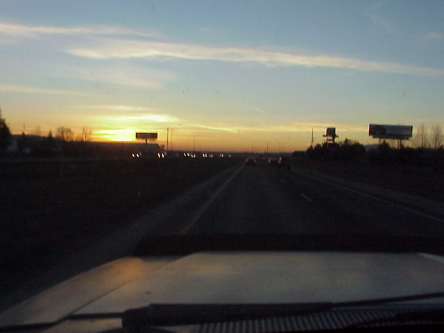 driving on highway during sunset, cars in distance, billboards visible