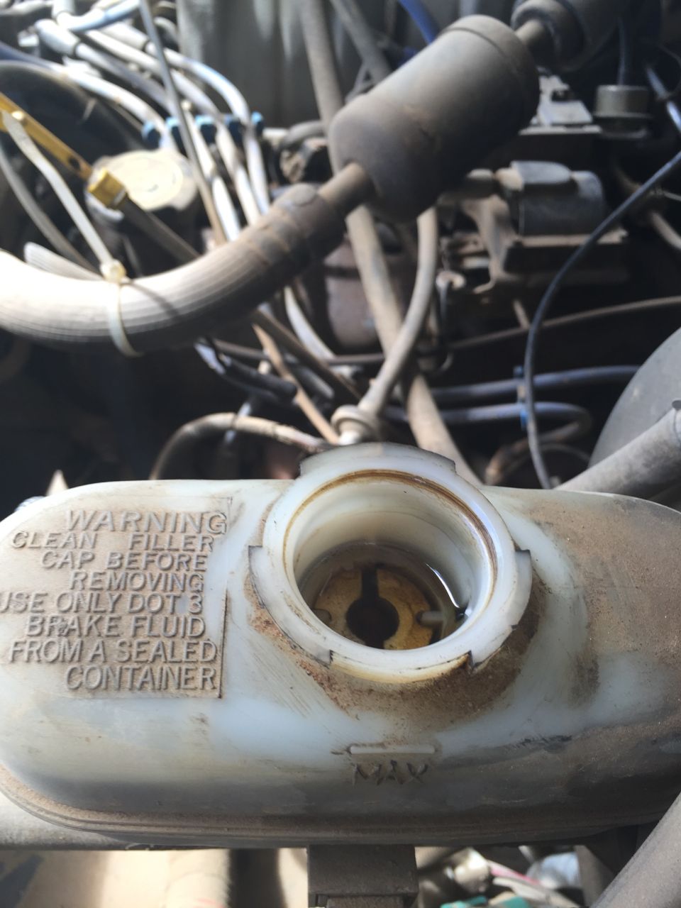 Close-up of brake fluid reservoir with warning text. Engine components visible in background