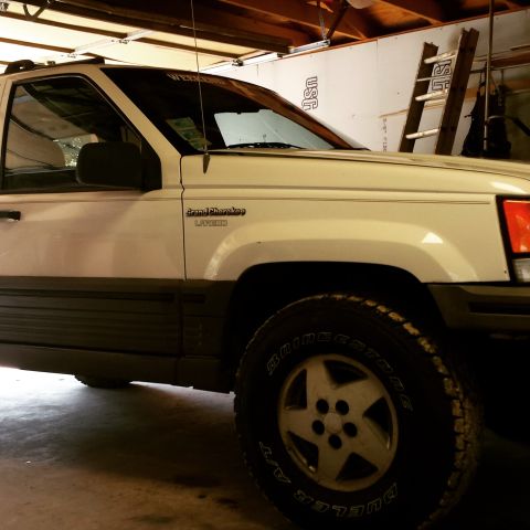 1994 Jeep Grand Cherokee - A white Jeep Grand Cherokee Laredo is parked inside a garage, showing its front quarter panel and wheel.