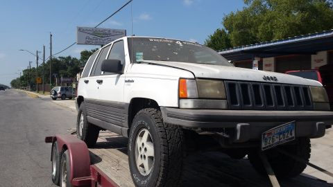 1994 Jeep Grand Cherokee - A white Jeep Grand Cherokee is loaded onto a trailer, parked on the side of a road.
