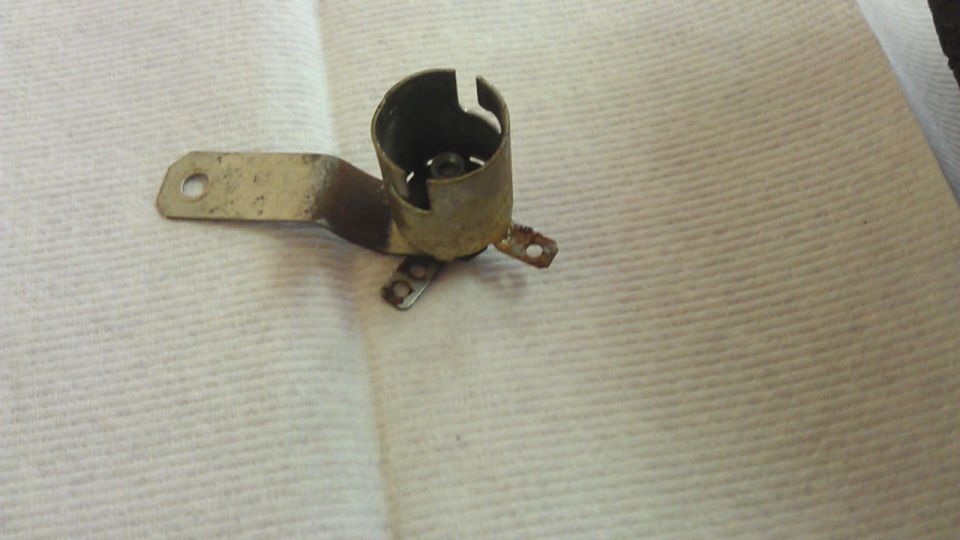 Metal light bulb socket with a mounting bracket, resting on a white textured surface