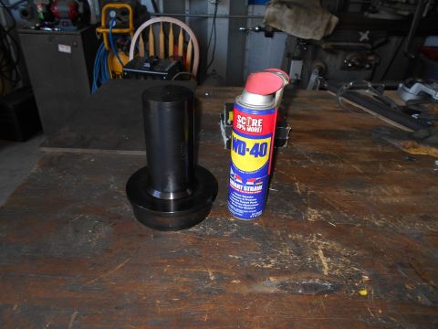 1992 Ford Bronco - A metal part and a can of WD-40 sit on a cluttered workbench in a garage or workshop.
