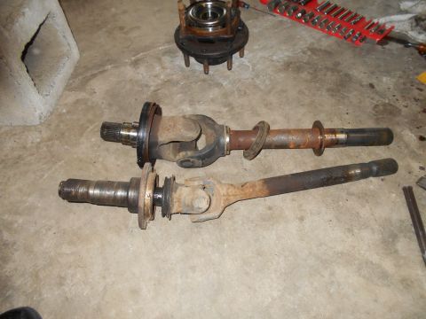 1992 Ford Bronco - Two rusty driveshafts and a front hub assembly are laid out on a concrete floor with tools in the background.