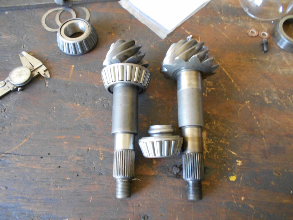 Two differential pinion gears with bearings and a separate bearing race on a wooden surface, with a caliper to the left