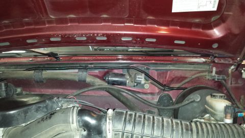 1996 Ford Bronco - Rear of the engine bay on a burgundy truck, looking at the cowl with the windshield wiper motor, its loom routed in a black plastic conduit…