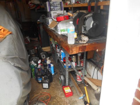 1994 Ford Bronco - A cluttered workbench in a garage contains a grinder, various bottles of fluids, and a large object covered by a tarp.